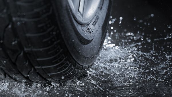 Nahaufnahme eines Autoreifens auf nasser Straße mit spritzendem Wasser