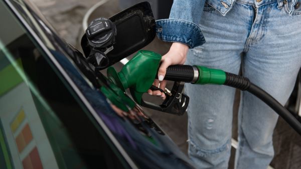 Eine Person, die eine grüne Zapfpistole hält, während sie ein Fahrzeug an einer Tankstelle betankt, zeigt die Nahaufnahme des Zapfsäulenmechanismus.