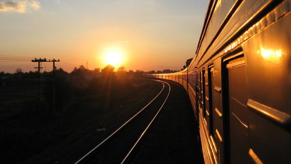 Der Blick entlang eines fahrenden Zuges in der Abendsonne vermittelt die ruhige Atmosphäre einer langen Bahnreise mit dem eigenen Auto.