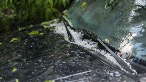 Hagelkörner und Blätter bedecken die nasse Windschutzscheibe eines Autos nach einem Unwetter.