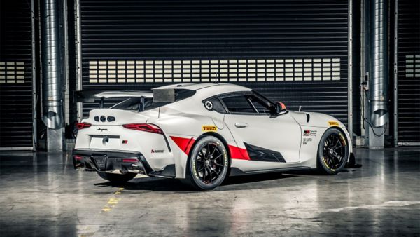 Ein schnittiger weißer GR Supra GT4 mit roten und schwarzen Akzenten, der in einer Garage mit industrieller Kulisse geparkt ist und sein Heckprofil und sein aerodynamisches Design zur Schau stellt.