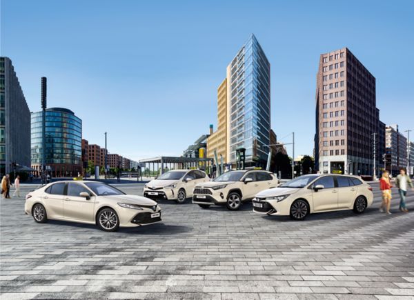 Vier beige Taxi Modelle, die auf einem städtischen Platz geparkt sind, mit hohen Gebäuden im Hintergrund.