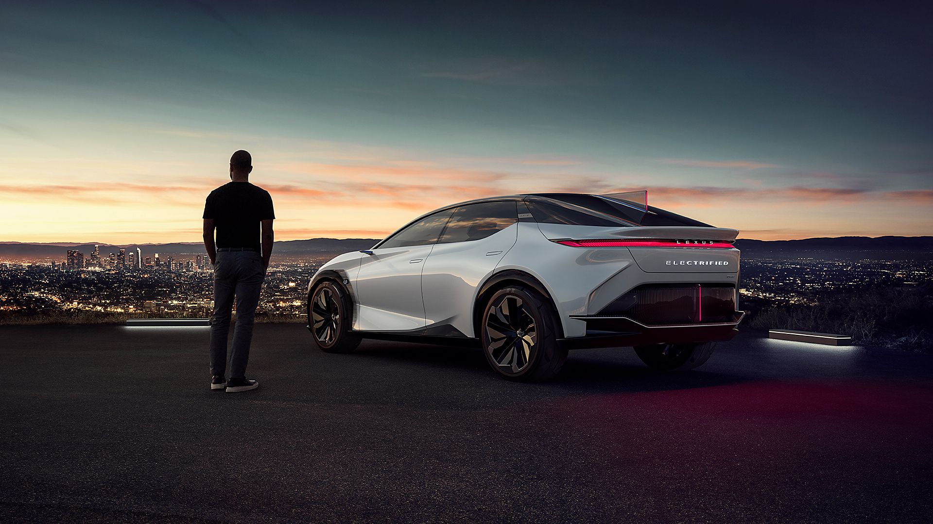 Eine Person steht neben einem Lexus Wagen im Sonnenuntergang
