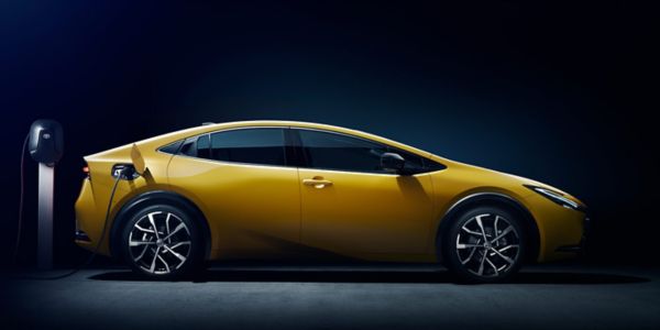 Seitenansicht eines gelben Prius Plug-in Hybrid angeschlossen an einer Toyota Ladesäule vor dunklem Hintergrund.