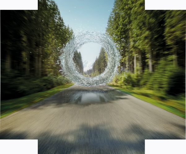 Dynamisches Foto einer Straße durch einen Wald, im Mittelpunkt hineinretuschiert ein runder Wasserstrudel, durch den Berge am Horizont erkennbar sind