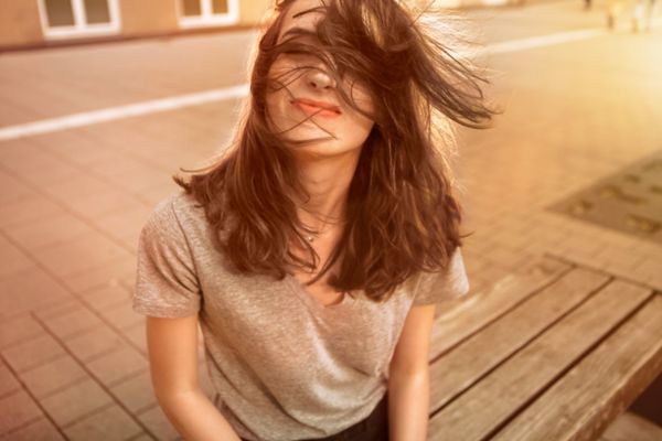 Eine Frau, die auf einer Bank sitzt und ihre Haare im Gesicht hat aufgrund von wehendem Wind.