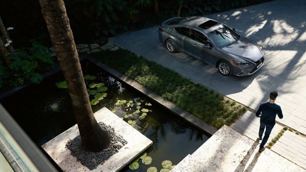Eine Person verlässt ein Gebäude und geht auf einen am Straßenrand geparkten Lexus zu