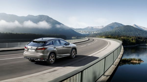 Ein silberner Lexus RX fährt über eine Brücke mit einer Stadt-Silhouette im Hintergrund