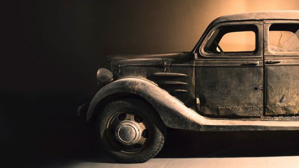 Ein rustikales Oldtimer-Auto mit verwittertem Äußeren, das seine antiken Merkmale vor einem dunklen Hintergrund hervorhebt.