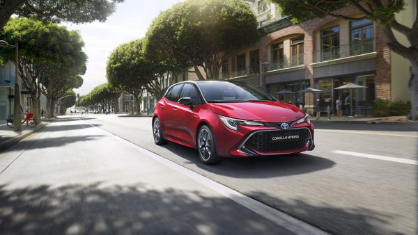 Roter Toyota Corolla fährt über eine mit Bäumen gesäumte Straße in einer Innenstadt