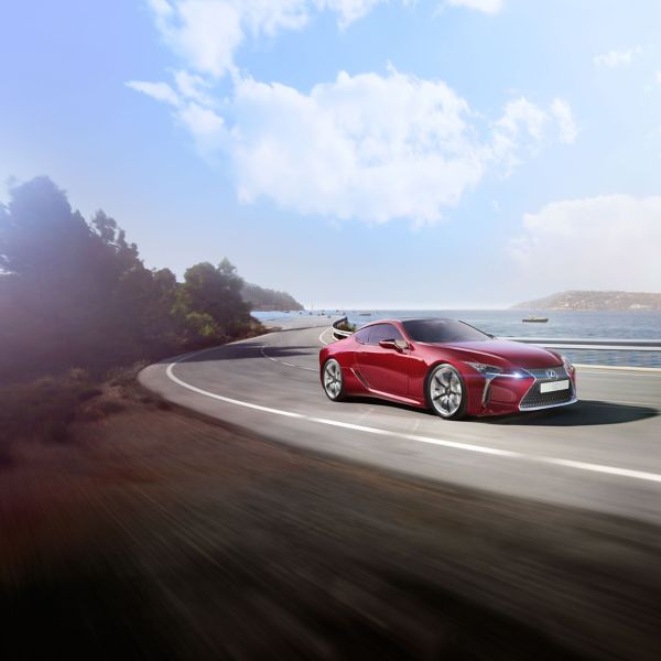 Ein roter Lexus LC fährt eine sonnige Küstenstraße entlang