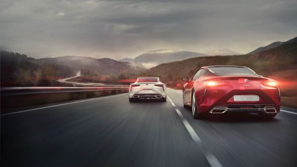 Ein weißer und ein roter Lexus fahren in der Dämmerung eine kurvige Bergstraße entlang
