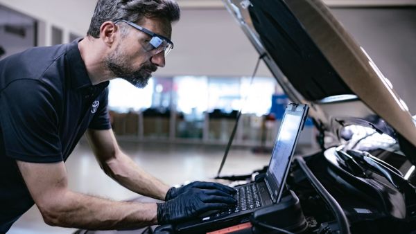 Ein Toyota-Werkstattmitarbeiter in grau-roter Arbeitskleidung gießt Öl in den Motor eines weißen Toyotafahrzeugs.