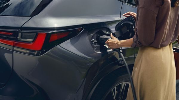 Eine Person schließt ein Ladekabel für ein Elektrofahrzeug an einen grauen Lexus an.