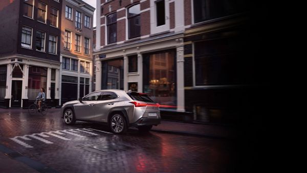 Silberner Lexus fährt durch die Gassen einer verregneten Stadt