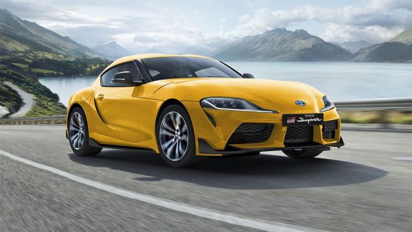 Gelber Toyota GR Supra fährt eine Küstenstraße neben einem See entlang