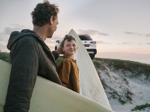 Vater und Sohn stehen mit Surfbrettern am Strand, im Hintergrund parkt ein weißer SUV von Toyota