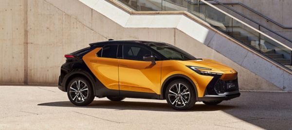 Orange-schwarzer Toyota C-HR steht geparkt in der Sonne neben einer Treppe