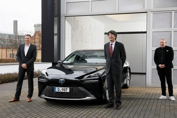 Drei Personen stehen vor einer Lagerhalle, eine davon ist Generalkonsul Kiminori Iwama vor seinem Toyota Mirai