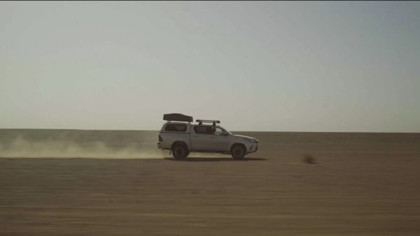 Ein weißer Pick-up Truck von Toyota mit einem Dachzelt fährt durch eine kahle Wüste