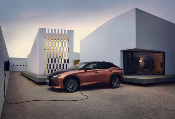 Ein eleganter Lexus RZ ist vor einem modernen Haus geparkt und an eine Ladestation angeschlossen, die zeitgenössische Architektur und einen minimalistischen Stil präsentiert.