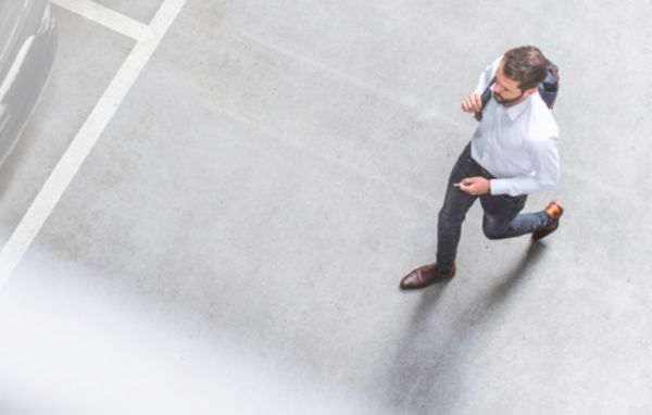 Eine Person in Business-Klamotten läuft über einen leeren Parkplatz