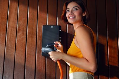 Person steht vor einer Toyota HomeCharge Wallbox mit einem Ladestecker in der Hand.