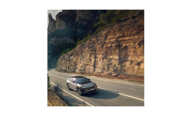 Ein silbergrauer Toyota bZ4X fährt auf einer Straße durch eine felsige Landschaft, erhöht von vorn dynamisch fotografiert