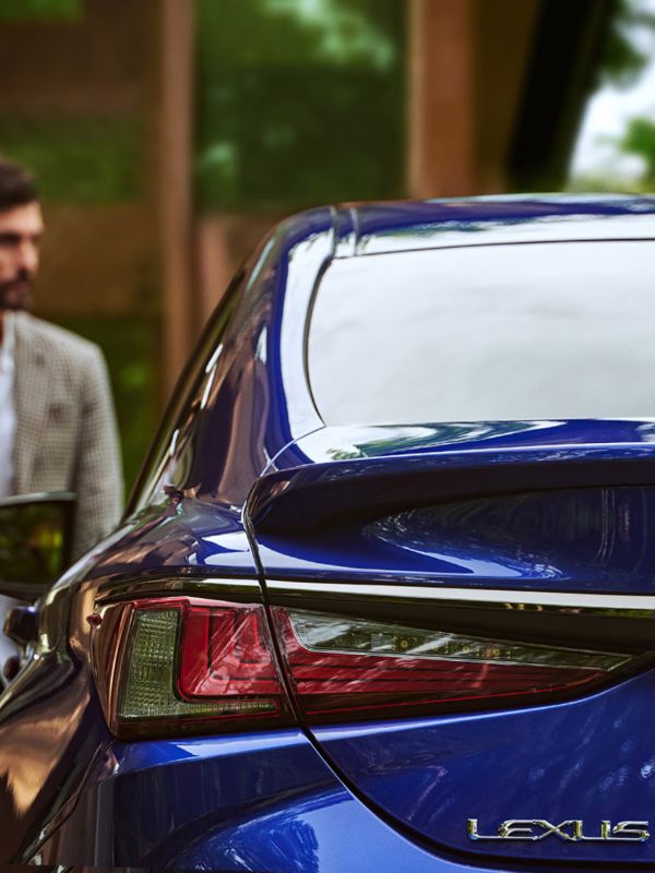 Eine Person geht auf einen im Schatten geparkten Lexus zu