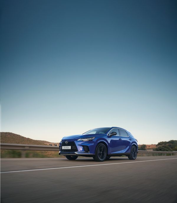 Ein blauer Lexus SUV fährt unter freiem Himmel über eine malerische Landstraße und präsentiert sein elegantes Design und seine moderne Ausstattung.