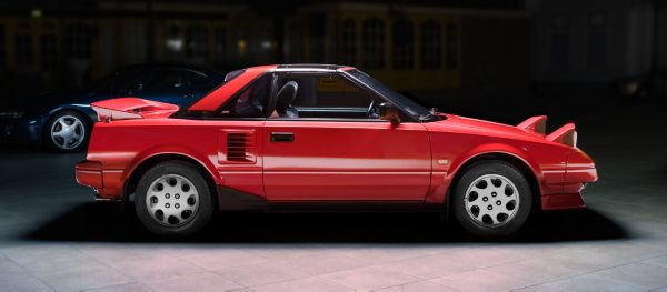 Seitenansicht eines roten Toyota MR2 mit hochgeklappten Scheinwerfern im Spot-Licht in einer abgedunkelten Ausstellungshalle