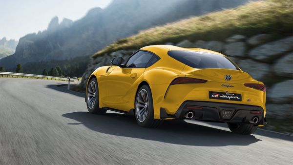 Gelber Toyota GR Supra von schräg hinten fährt eine kurvige Bergstraße entlang