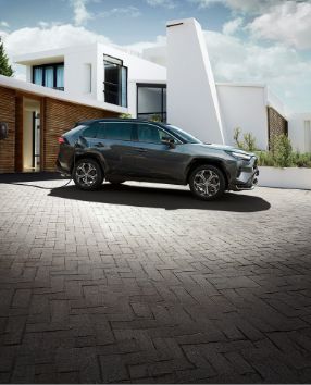 Toyota RAV4 Plug-in Hybrid stoi pod willą i ładuje baterie ze stacji domowej.