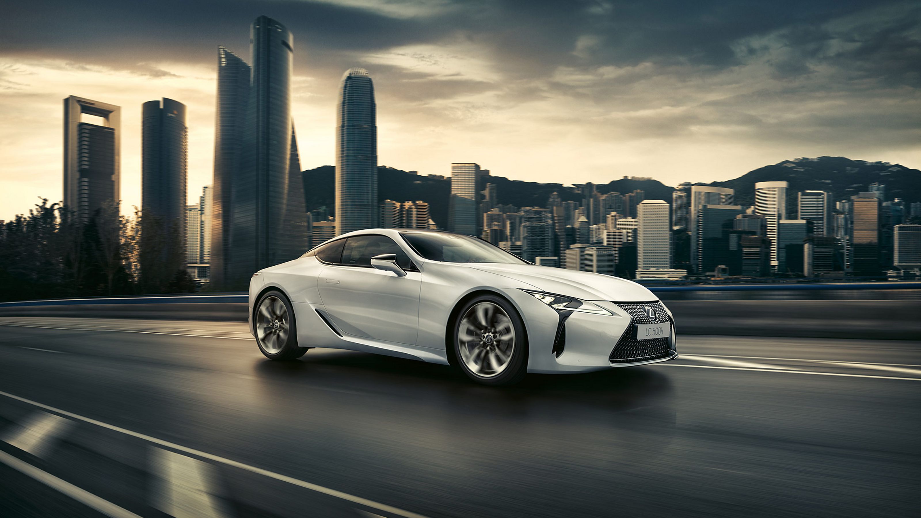 Ein Lexus LC fährt auf einer Straße an einer Stadt vorbei