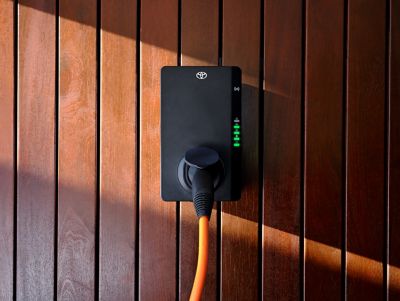 Eine mit Toyota gebrandete Wallbox hängt einer Holzwand, ein orangenes Kabel hängt daran.