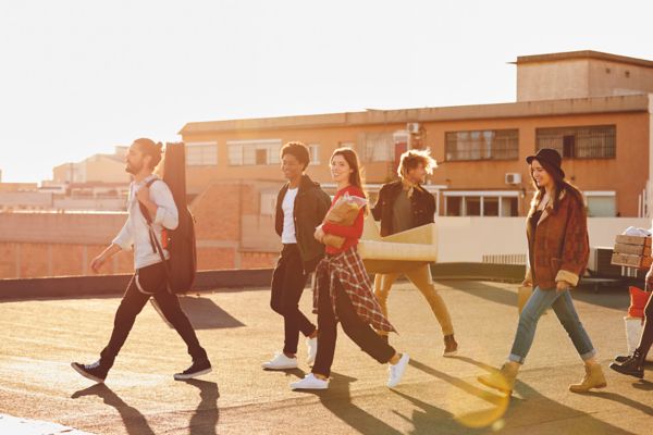 Eine Gruppe von fünf jungen Erwachsenen, die bei Sonnenuntergang gemeinsam auf einem Dach spazieren gehen, in Freizeitkleidung und mit glücklichen Gesichtern.