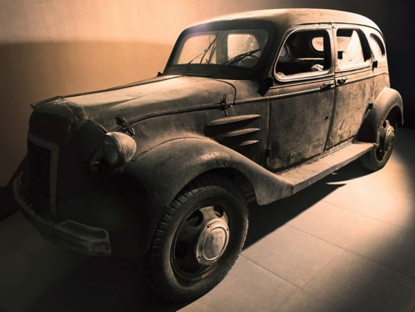 Extrem verwitterter und staubiger Toyoda AA von 1936 mit teilweise zerbrochenen Scheiben von schräg vorn in einem gefliesten Ausstellungsraum