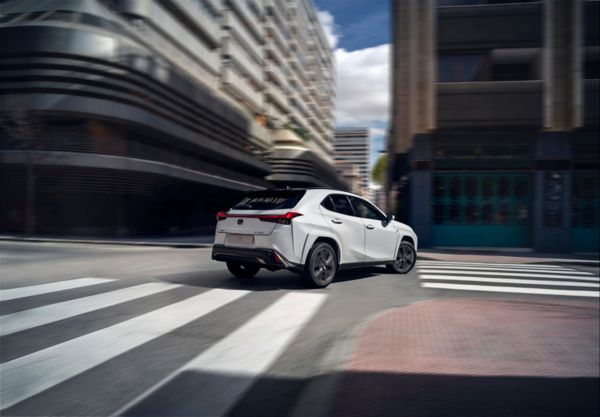 Ein eleganter weißer Lexus SUV biegt an einem städtischen Zebrastreifen nach links ab, mit modernen Gebäuden im Hintergrund unter einem teilweise bewölkten Himmel.
