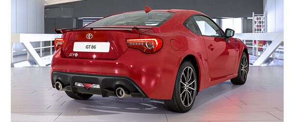Ein roter Toyota GT86 mit leuchtenden Rücklichtern von schräg hinten in einer Ausstellungshalle
