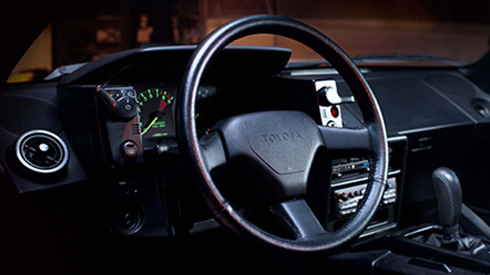 Cockpit des Toyota MR2 mit Lederlenkrad, schwarzen Armaturen und einem grün leuchtenden Tachometer
