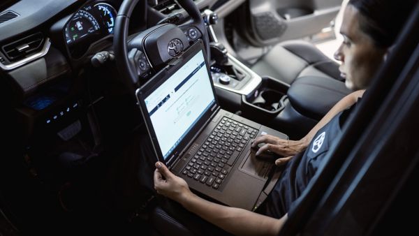 Person mit Laptop auf dem Schoß sitzt auf Fahrersitz und diagnostiziert die Fahrzeugwerte