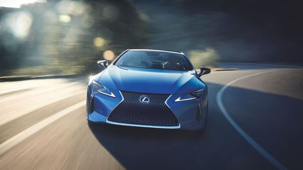Ein blauer Lexus LC fährt auf einer Schnellstraße, beleuchtet von strahlendem Sonnenschein