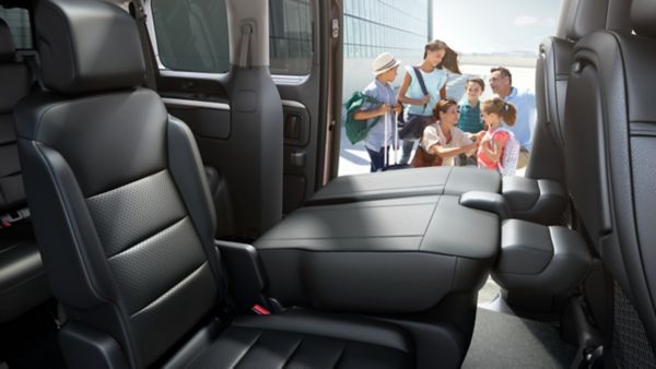Toyota Proace Verso Innenansicht auf die umgeklappte hintere Sitzreihe, im Hintergrund eine Familie mit Gepäck.
