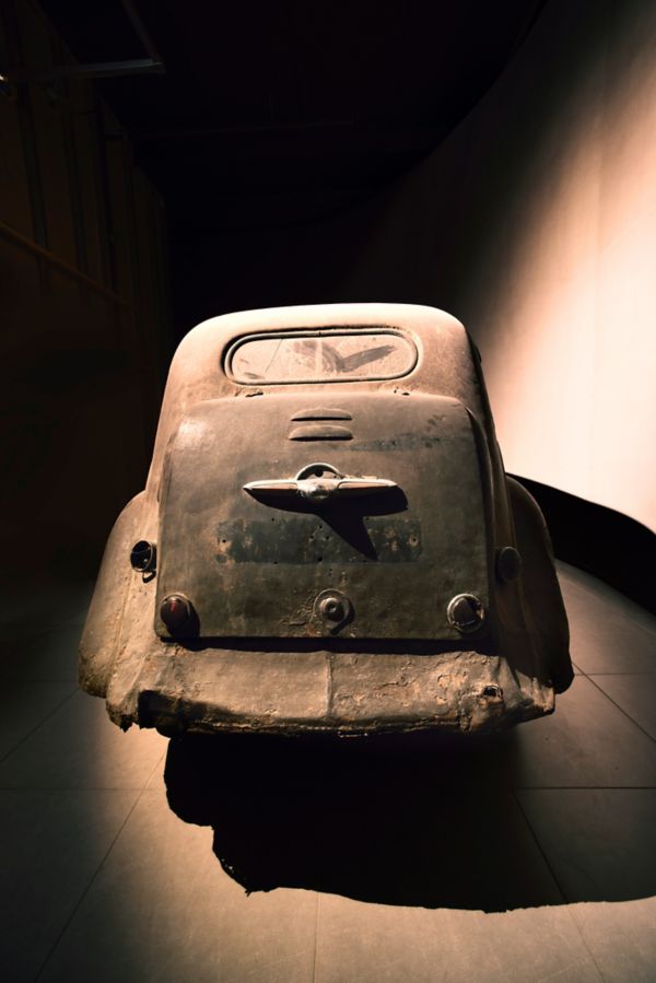 Rückansicht eines extrem verwitterten und staubigen Toyoda AA von 1936, punktuell beleuchtet in einem abgedunkelten Ausstellungsraum