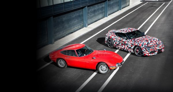 Ein roter Toyota 2000GT von 1967 und ein GR Supra mit auffälligem schwarz-weiß-roten Muster nebeneinander in der Boxengasse einer Rennstrecke geparkt