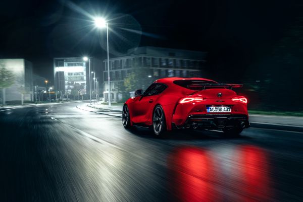 Roter Toyota Supra fährt über eine nasse Stadt-Straße in der Nacht