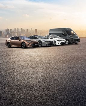 Na tle miasta stoją cztery Toyoty: Camry, Prius, Corolla i PROACE Max.