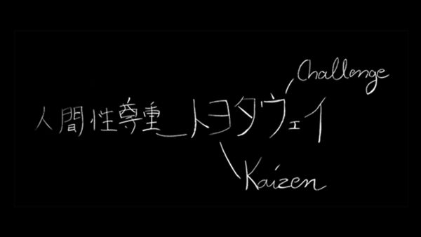 Das Bild zeigt einen handgeschriebenen Text mit japanischen Schriftzeichen und englischen Wörtern. Der japanische Text lautet "Respekt vor der menschlichen Natur" und "Toyota", begleitet von den englischen Wörtern „Challenge“ und „Kaizen“.