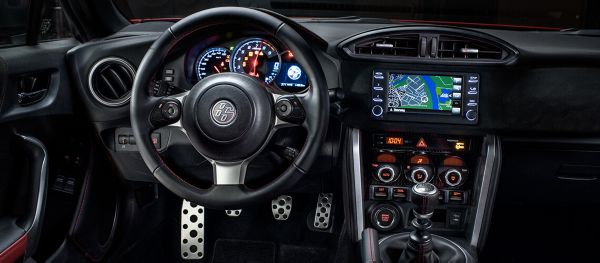 Lenkrad und Armaturenbrett des Toyota GT86 mit leuchtenden Schaltern, aktivem Fahrer-Display und einer Kartenansicht auf dem Multimedia-Bildschirm