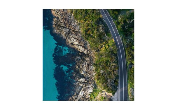 Luftaufnahme eines Kliffs, rechts verläuft eine Straße, links erstreckt sich das blaue Meer.